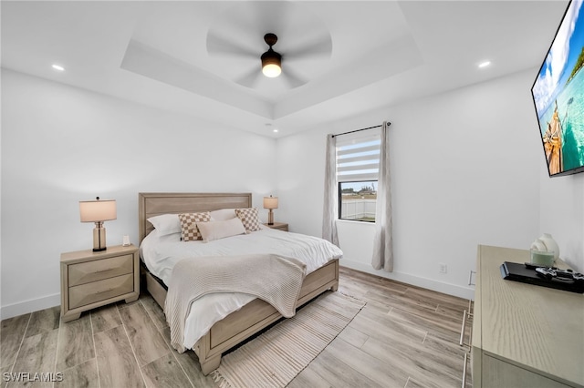 bedroom with a raised ceiling, light hardwood / wood-style floors, and ceiling fan