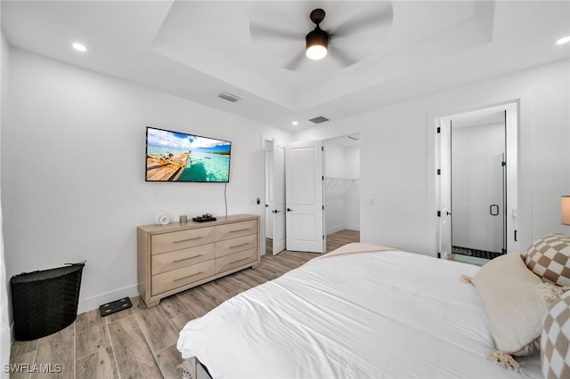 bedroom with a closet, a walk in closet, a tray ceiling, light hardwood / wood-style floors, and ceiling fan