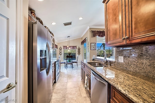 kitchen featuring light stone countertops, vaulted ceiling, stainless steel appliances, sink, and decorative light fixtures