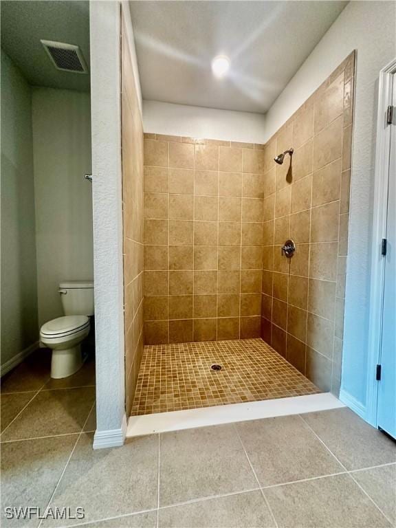 bathroom featuring a tile shower, tile patterned floors, and toilet