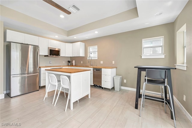 kitchen featuring a center island, appliances with stainless steel finishes, white cabinetry, a kitchen bar, and butcher block counters