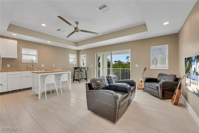 living room with a tray ceiling, a wealth of natural light, and ceiling fan