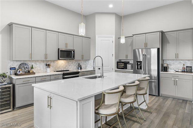 kitchen with a kitchen island with sink, a towering ceiling, hanging light fixtures, and appliances with stainless steel finishes