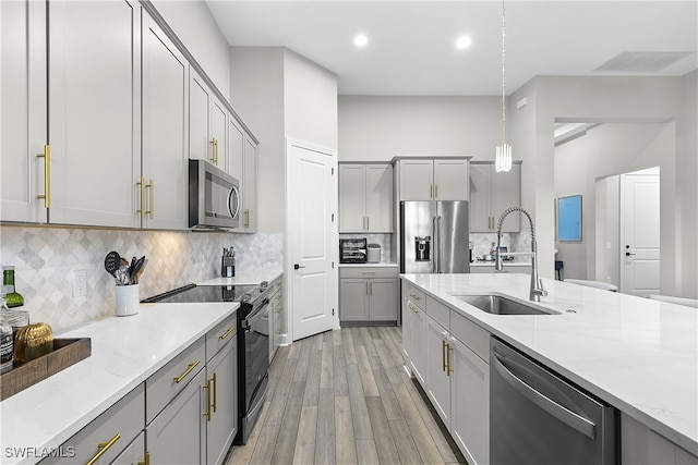 kitchen with gray cabinetry, sink, hanging light fixtures, decorative backsplash, and stainless steel appliances