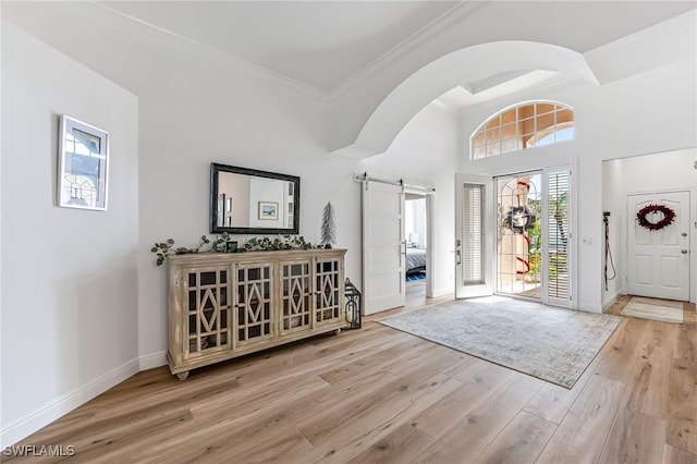 foyer entrance with a barn door, light hardwood / wood-style floors, and ornamental molding