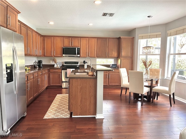 kitchen featuring a center island with sink, sink, stainless steel appliances, pendant lighting, and dark hardwood / wood-style floors