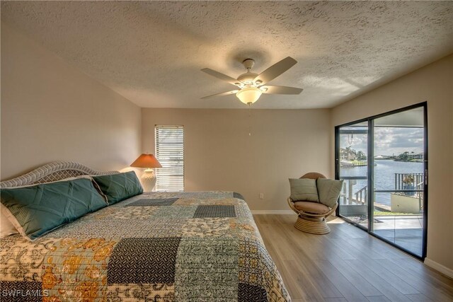 bedroom with access to outside, a textured ceiling, multiple windows, ceiling fan, and a water view