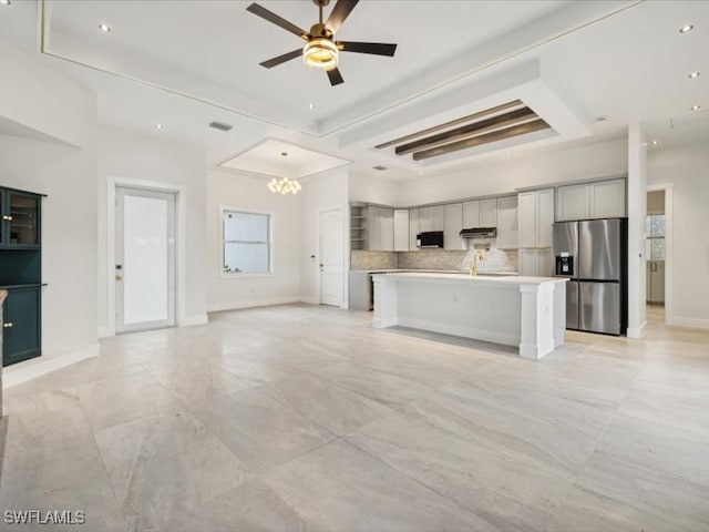 kitchen featuring appliances with stainless steel finishes, a kitchen breakfast bar, backsplash, range hood, and a kitchen island with sink