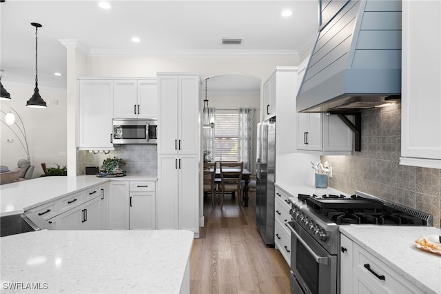 kitchen with pendant lighting, white cabinets, appliances with stainless steel finishes, and premium range hood