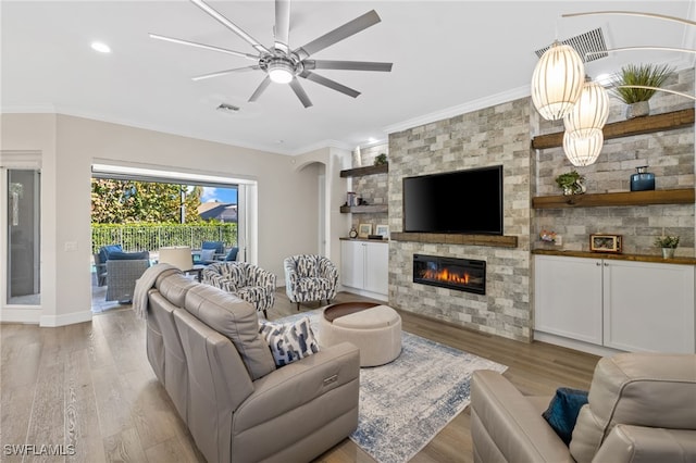 living room with ceiling fan with notable chandelier, light hardwood / wood-style floors, ornamental molding, and a stone fireplace