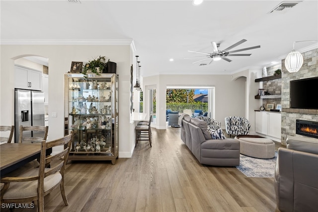 3684 Sudbury Ln, Bonita Springs, FL 34134 - living room with arched walkways, a fireplace, light wood-style flooring, ceiling fan, and ornamental molding