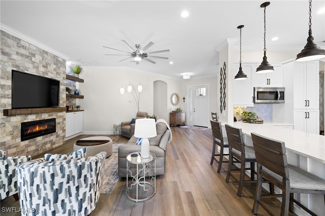 living room featuring wood-type flooring, a stone fireplace, crown molding, and ceiling fan