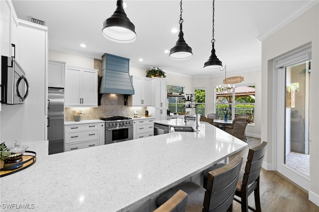 kitchen with premium appliances, white cabinetry, hanging light fixtures, and custom exhaust hood