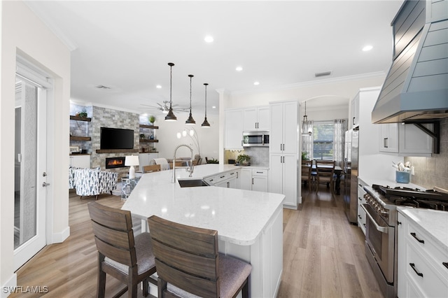 kitchen featuring white cabinets, premium range hood, hanging light fixtures, stainless steel appliances, and a breakfast bar area