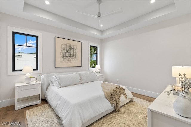 bedroom with hardwood / wood-style floors, multiple windows, a tray ceiling, and ceiling fan