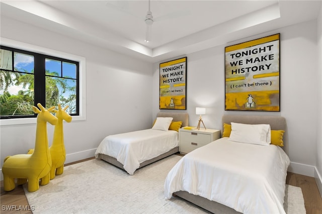 bedroom with ceiling fan, a raised ceiling, and light hardwood / wood-style flooring