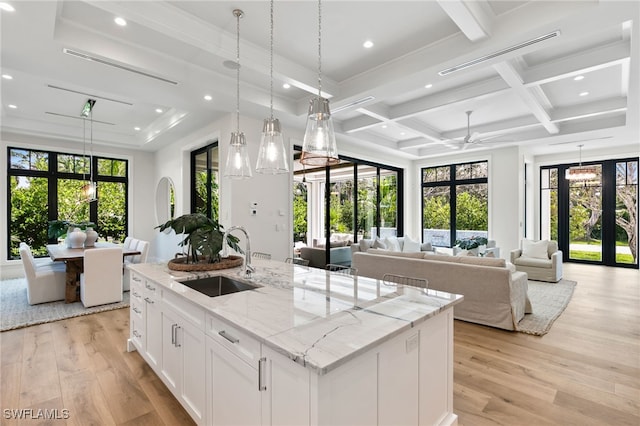 kitchen with white cabinetry, sink, light wood-type flooring, and a center island with sink