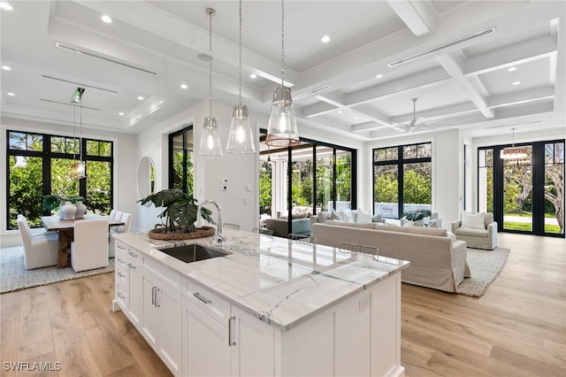 kitchen with a sink, a center island with sink, white cabinetry, and open floor plan