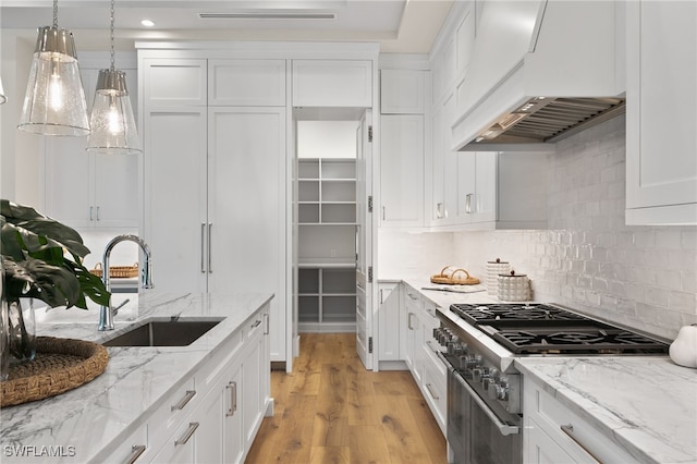 kitchen featuring high end stove, light hardwood / wood-style flooring, sink, custom exhaust hood, and white cabinets