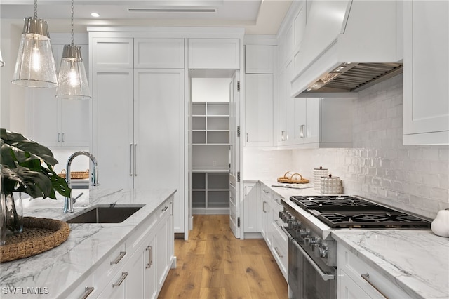 kitchen featuring custom exhaust hood, stainless steel stove, light wood-type flooring, white cabinetry, and a sink