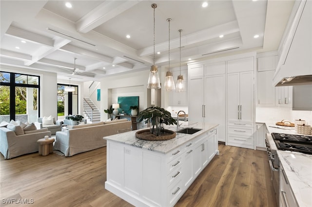 kitchen with wood finished floors, beam ceiling, premium range hood, a sink, and coffered ceiling