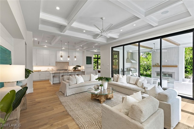 living area with ceiling fan, coffered ceiling, light wood-style flooring, and a wealth of natural light
