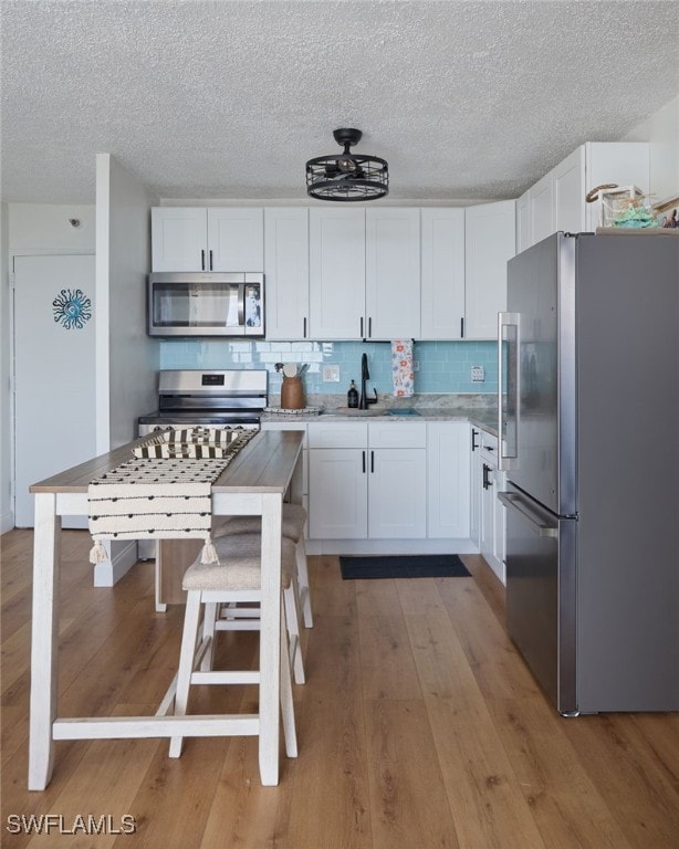 kitchen with white cabinetry, stainless steel appliances, light wood-type flooring, a kitchen bar, and sink