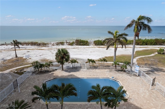 view of swimming pool with a patio, a water view, and a view of the beach