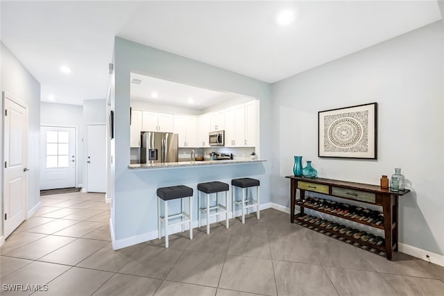 kitchen featuring appliances with stainless steel finishes, light tile patterned flooring, light stone counters, white cabinets, and kitchen peninsula