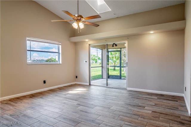 spare room featuring ceiling fan, a skylight, light hardwood / wood-style flooring, and high vaulted ceiling