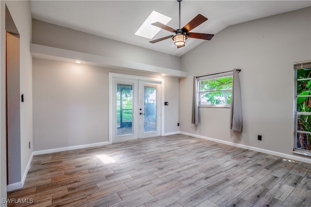 empty room with french doors, light hardwood / wood-style floors, ceiling fan, and lofted ceiling with skylight