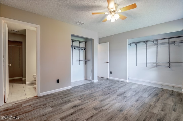 unfurnished bedroom with light hardwood / wood-style floors, a closet, a textured ceiling, ceiling fan, and ensuite bath