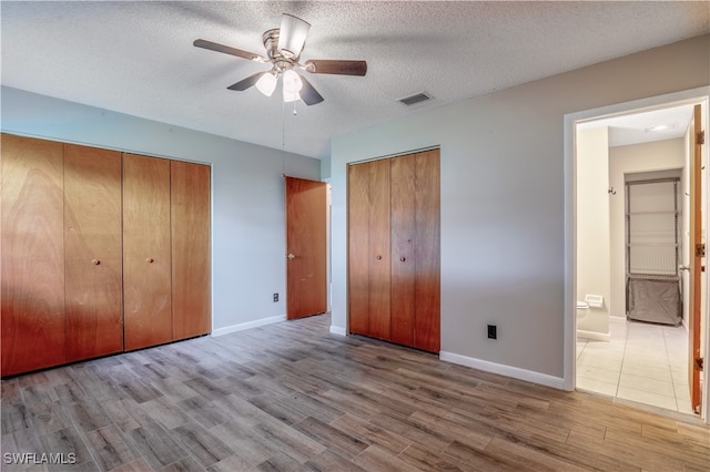 unfurnished bedroom with ceiling fan, a textured ceiling, light wood-type flooring, and ensuite bath