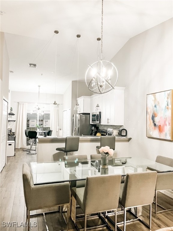 dining area with a chandelier, light hardwood / wood-style floors, and vaulted ceiling