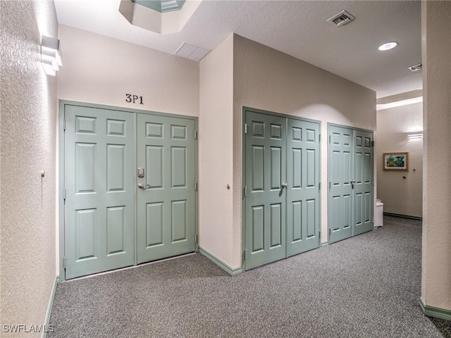 interior space with carpet floors, visible vents, a textured wall, a textured ceiling, and baseboards