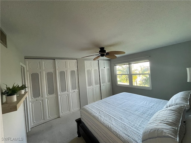 bedroom with ceiling fan, multiple closets, a textured ceiling, and light carpet