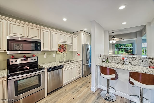 kitchen with light stone countertops, sink, cream cabinets, a kitchen bar, and appliances with stainless steel finishes