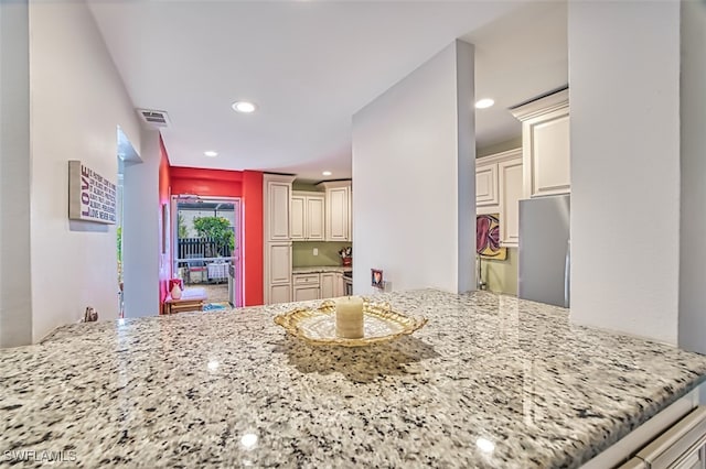 kitchen featuring stainless steel refrigerator, kitchen peninsula, light stone countertops, and cream cabinets