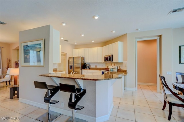 kitchen featuring appliances with stainless steel finishes, a kitchen breakfast bar, white cabinetry, kitchen peninsula, and stone countertops