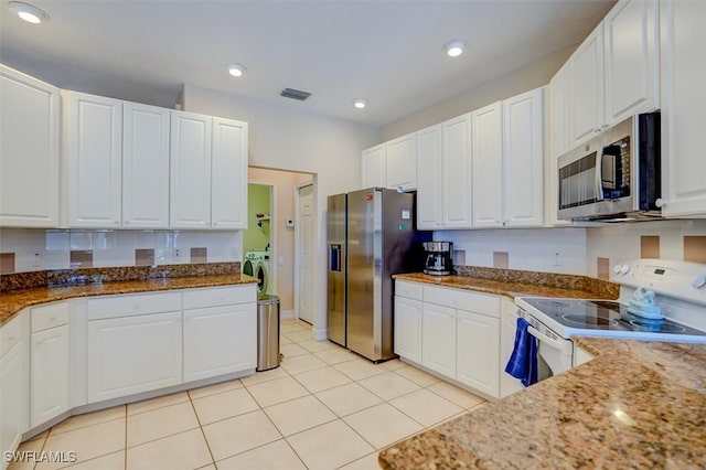 kitchen featuring light tile patterned flooring, white cabinetry, light stone counters, stainless steel appliances, and washer and clothes dryer