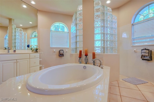 bathroom with plenty of natural light, tile patterned floors, tiled bath, and vanity