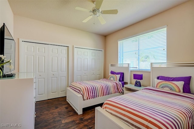 bedroom with a textured ceiling, ceiling fan, dark wood-type flooring, and multiple closets