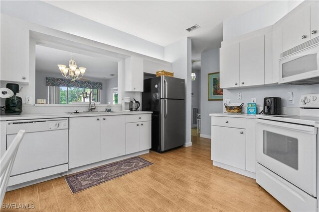 kitchen featuring white appliances, white cabinets, sink, hanging light fixtures, and a notable chandelier