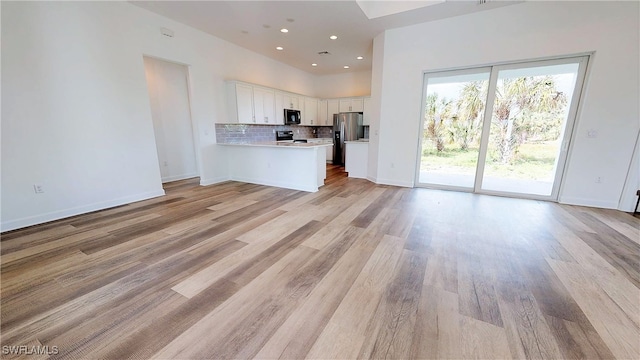 kitchen with decorative backsplash, light hardwood / wood-style floors, white cabinetry, kitchen peninsula, and stainless steel appliances