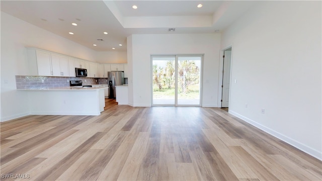 kitchen with appliances with stainless steel finishes, light hardwood / wood-style floors, white cabinetry, backsplash, and kitchen peninsula