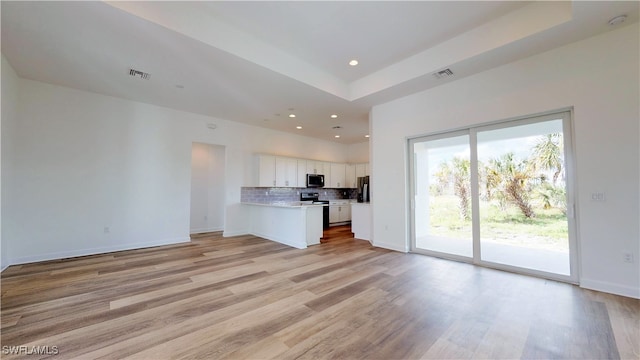 kitchen with decorative backsplash, light hardwood / wood-style floors, white cabinetry, a raised ceiling, and stainless steel appliances