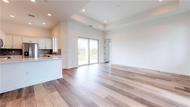 kitchen with stainless steel fridge, light hardwood / wood-style floors, white cabinetry, and a tray ceiling