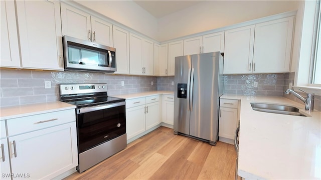 kitchen featuring appliances with stainless steel finishes, decorative backsplash, white cabinetry, light wood-type flooring, and sink