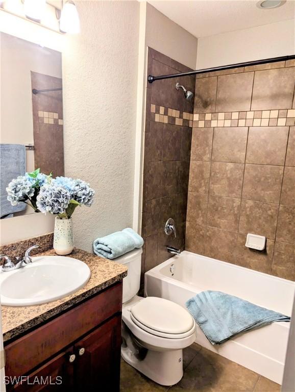 bathroom with shower / bathtub combination, a textured wall, toilet, vanity, and tile patterned flooring