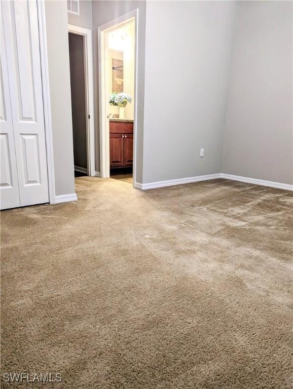 unfurnished bedroom featuring connected bathroom, light colored carpet, visible vents, baseboards, and a closet